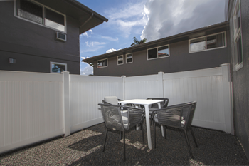 An oversized patio with a table and chairs in front of a white fence